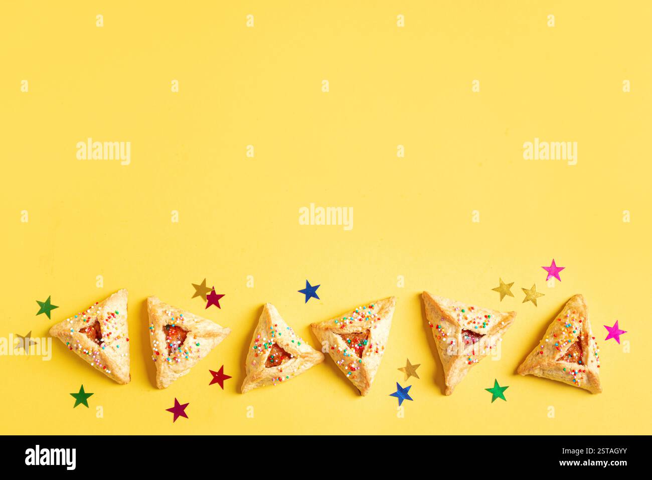 Purim Cookies Hamantaschen in Reihe mit Konfetti und Zuckerstreuseln auf gelbem Hintergrund, Kopierraum. Purim-Banner. Stockfoto