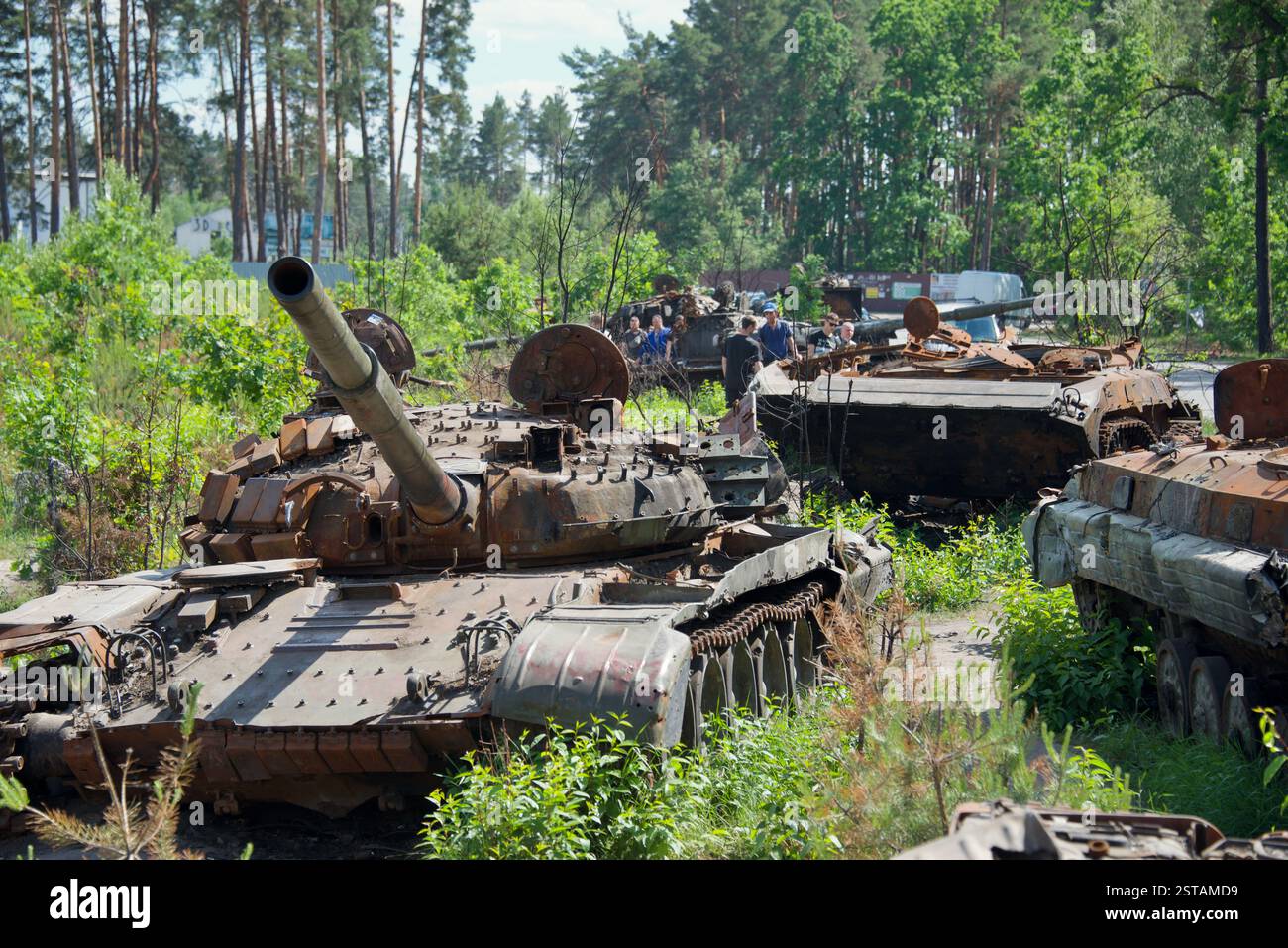 Die Bewohner betrachten gepanzerte Fahrzeuge, die am 8. Juni 2022 auf einem Panzerfriedhof in der Nähe von Bucha, Ukraine, gesammelt wurden. Stockfoto