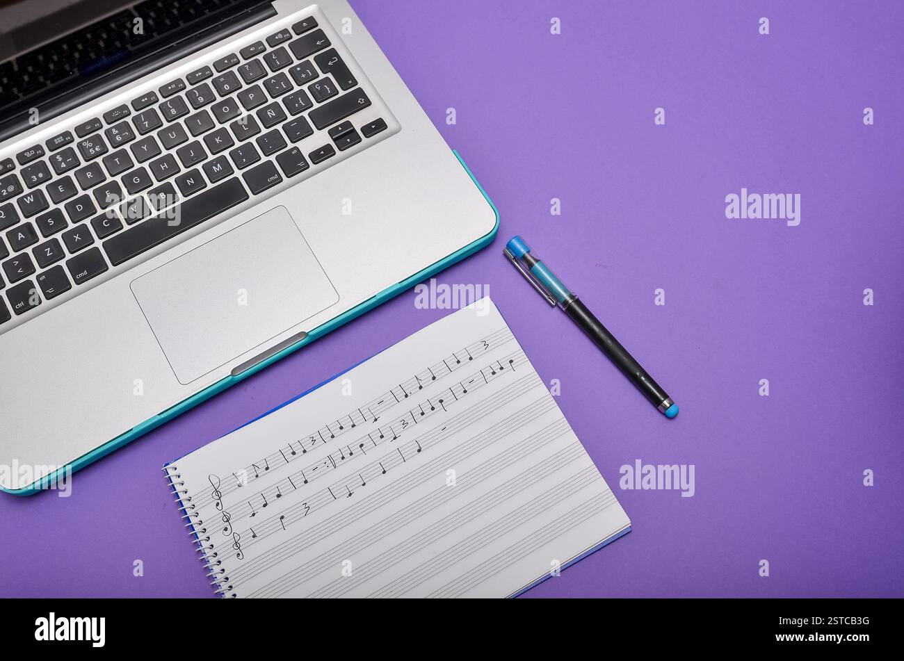 Musiknotizen werden auf einem Notizblock neben einem Laptop und einem Stift geschrieben, die auf Musikkomposition oder Online-Musikunterricht hinweisen Stockfoto
