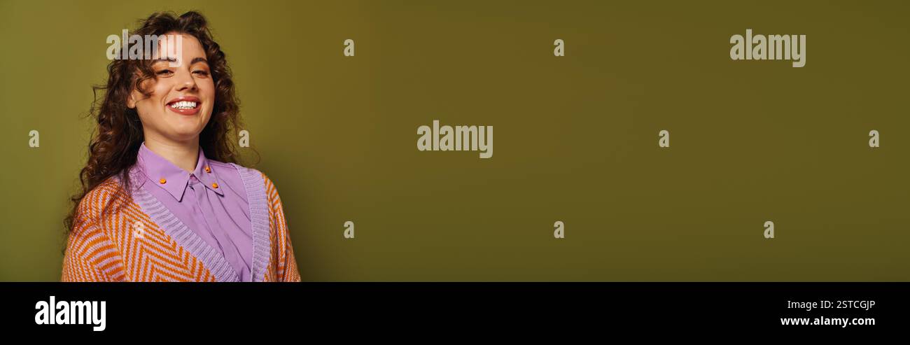 Eine junge Frau mit lockigem Haar präsentiert ihr trendiges Outfit in einem gemütlichen, stilvollen Raum. Stockfoto