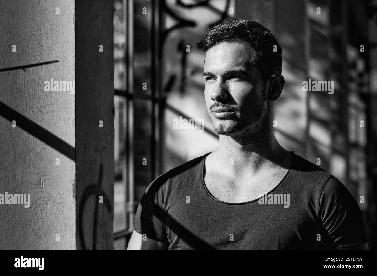 Schwarz-weiß-Porträt eines jungen Mannes drinnen neben Fenstern Stockfoto