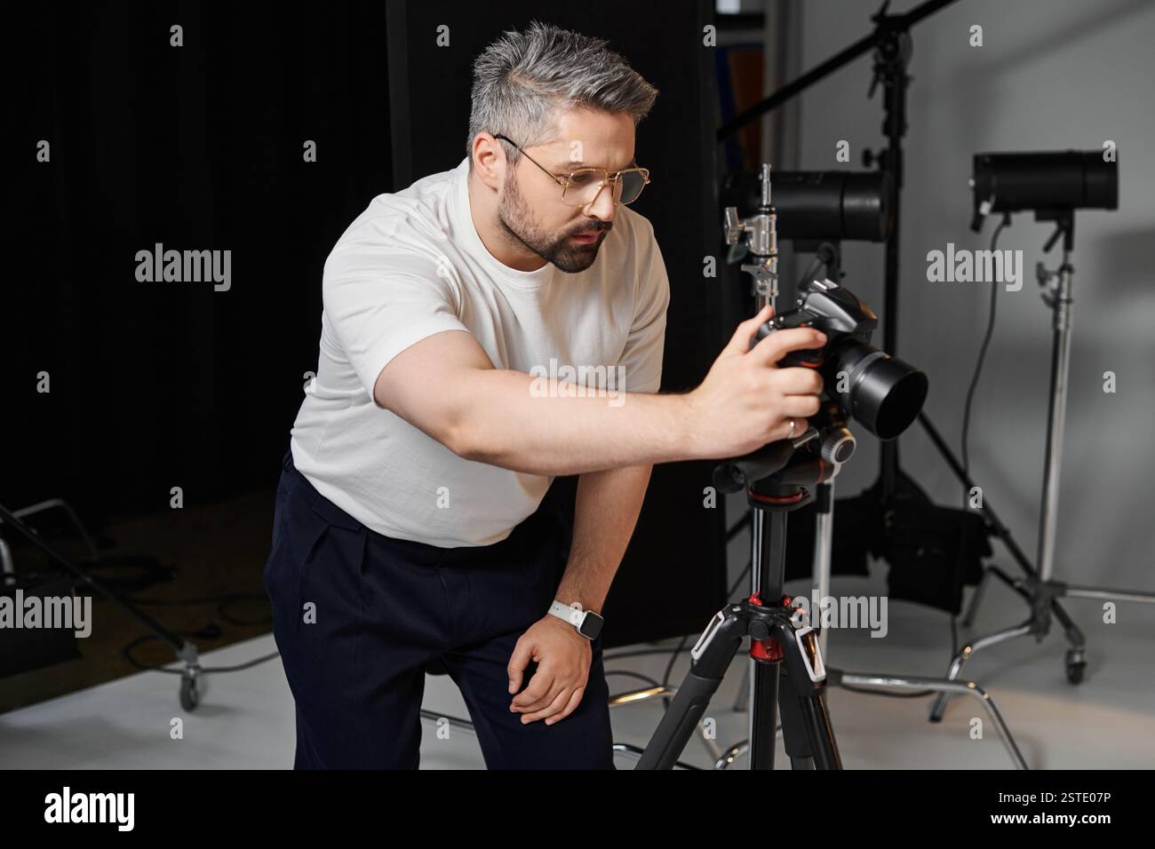 Ein engagierter Mann stellt seine Kamera auf einem Stativ auf, um atemberaubende Studioaufnahmen aufzunehmen. Stockfoto