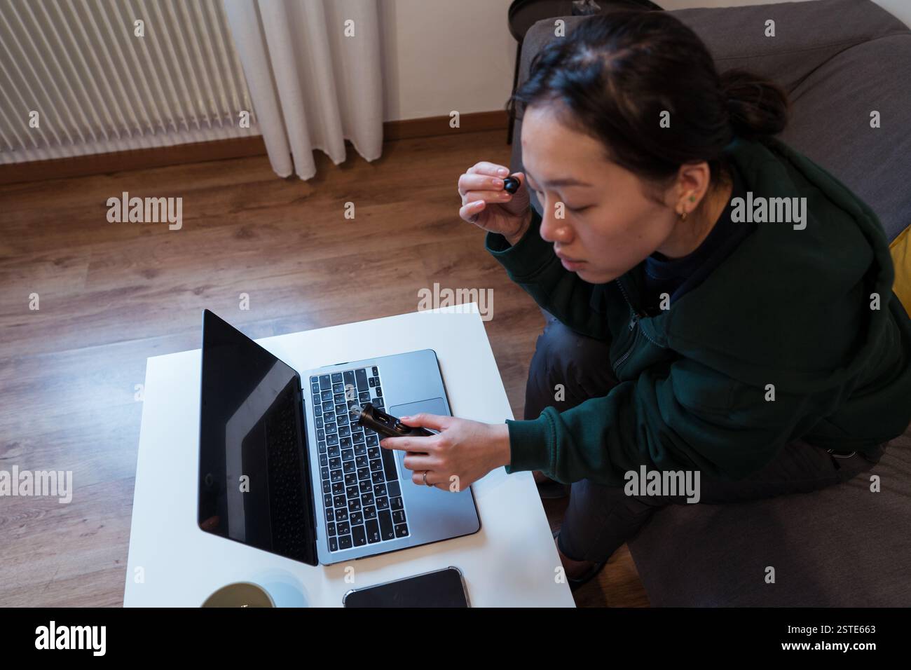 Eine fokussierte Frau verwendet eine Lupe, um den Bildschirm eines Laptops genau zu betrachten, was auf akribische Arbeit oder Untersuchung hindeutet Stockfoto
