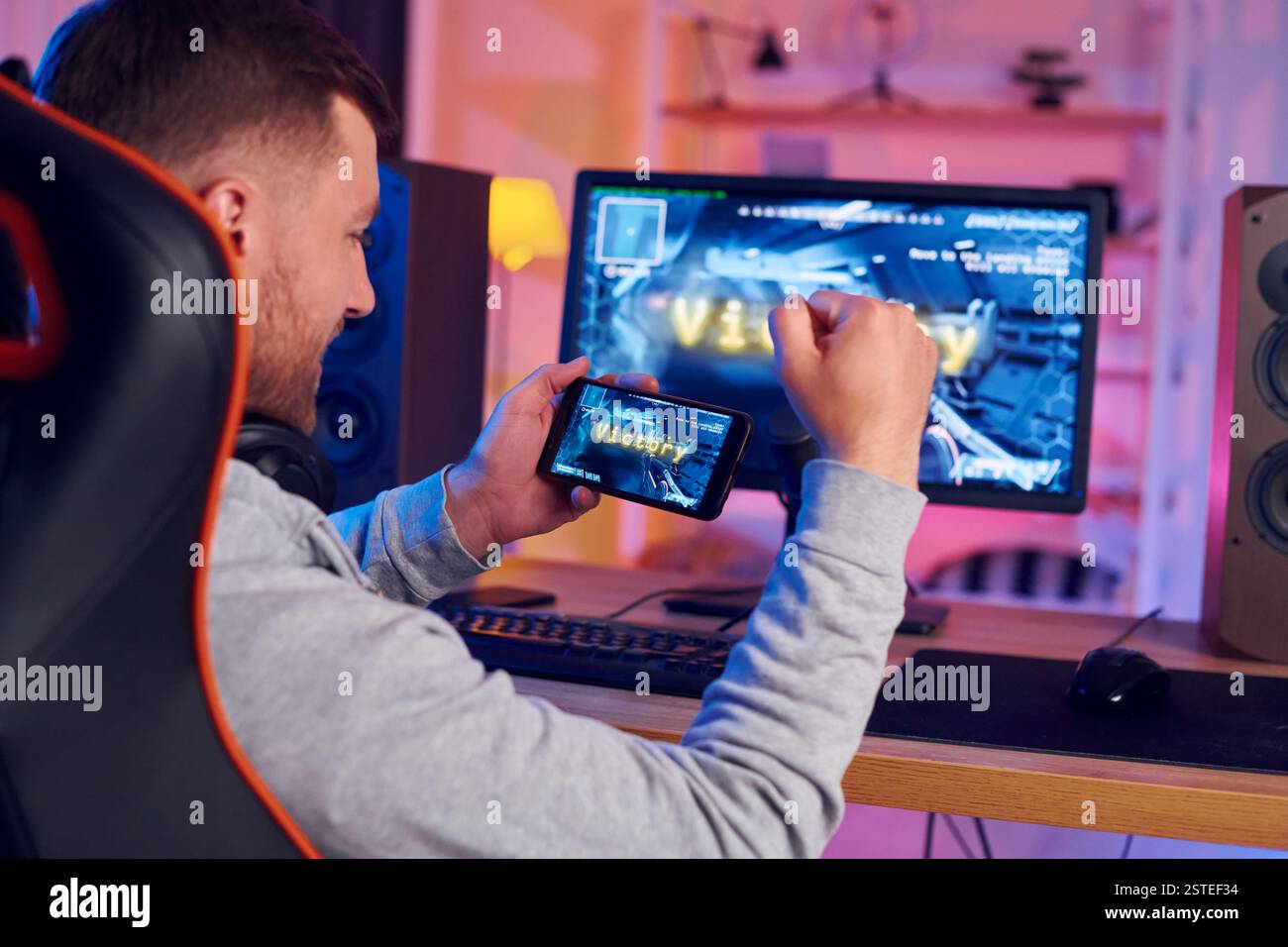 Smatphone halten und den Sieg feiern. Online-Streamer, der FPS-Shooter zu Hause spielt. Stockfoto