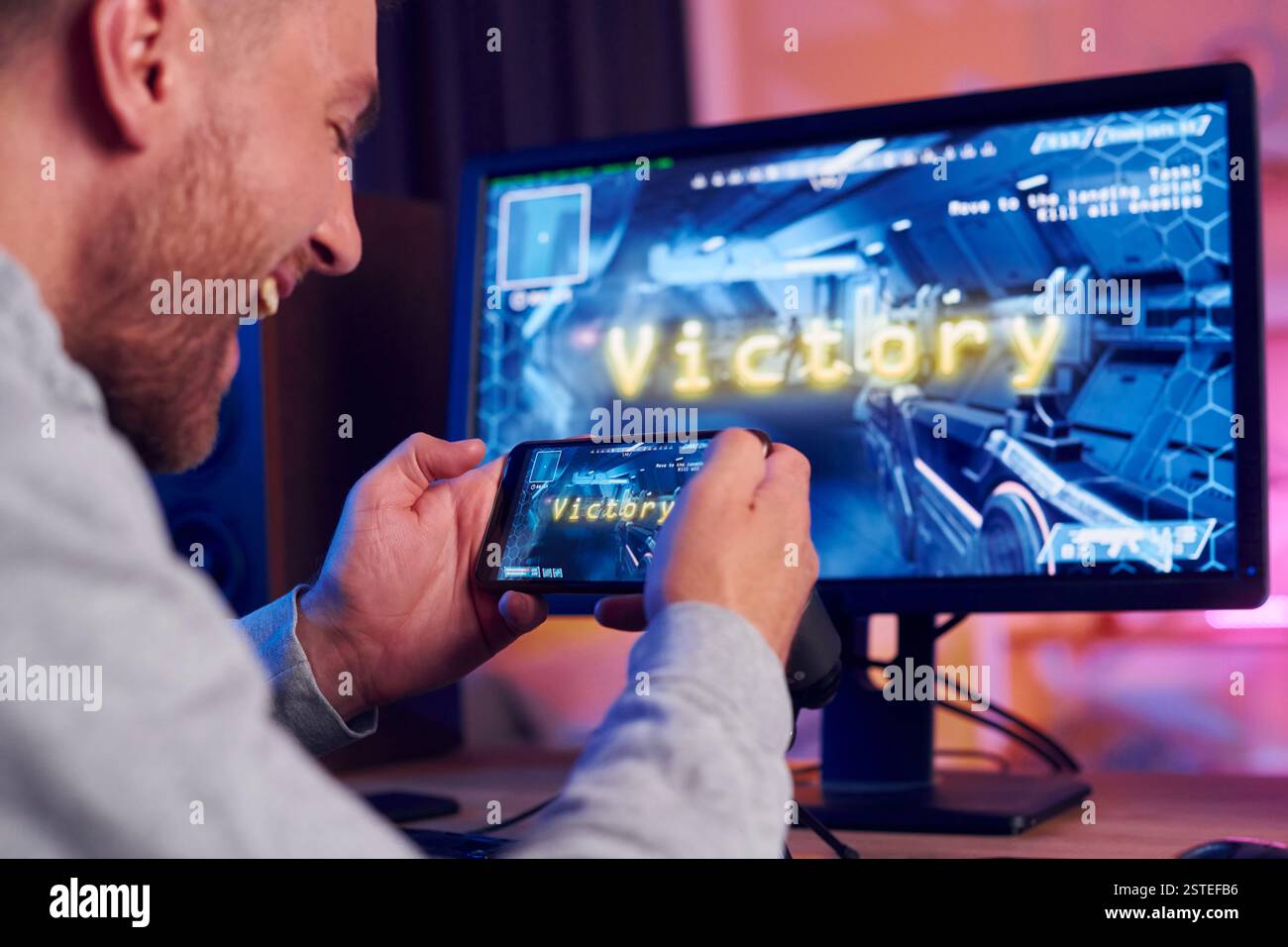 Smatphone halten und den Sieg feiern. Online-Streamer, der FPS-Shooter zu Hause spielt. Stockfoto
