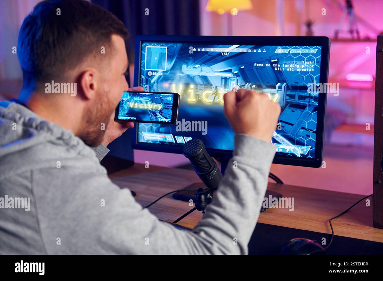 Anzeige des Monitors und des Smartphones. Online-Streamer, der FPS-Shooter zu Hause spielt. Stockfoto