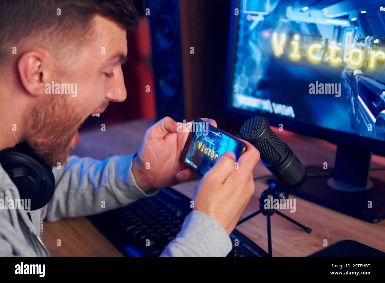 Anzeige des Monitors und des Smartphones. Online-Streamer, der FPS-Shooter zu Hause spielt. Stockfoto