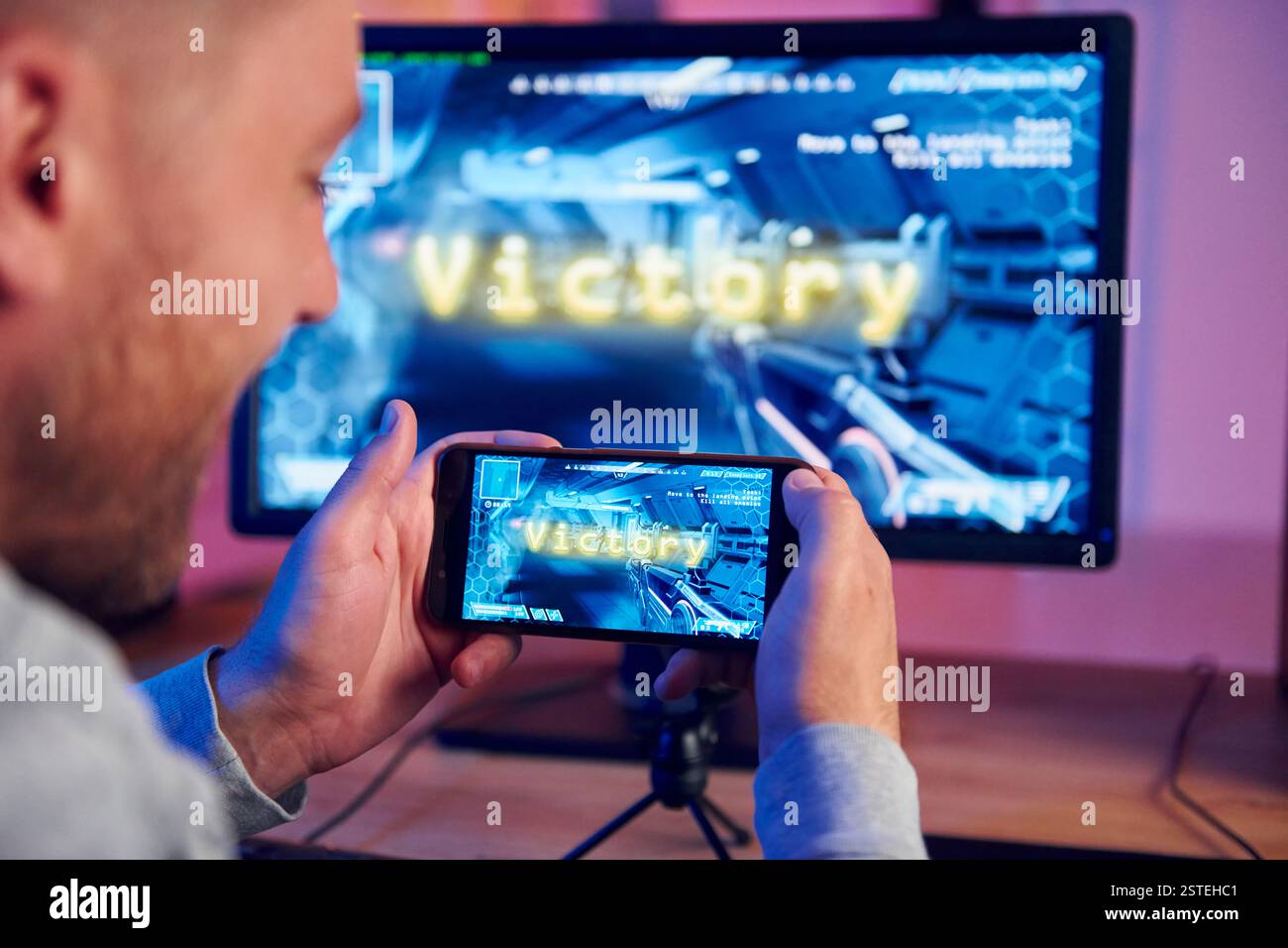 Anzeige des Monitors und des Smartphones. Online-Streamer, der FPS-Shooter zu Hause spielt. Stockfoto