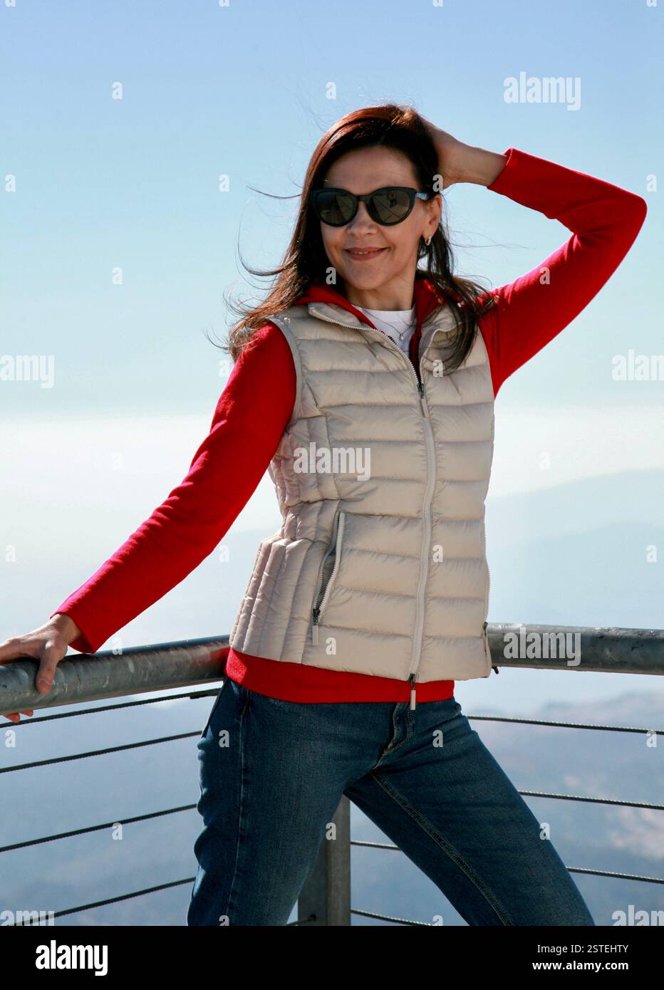 Zufriedene Frau 51 Jahre alt in sportlichem Outfit und Sonnenbrille posiert vor der Kulisse der Berge und des blauen Himmels Antalya Türkei Stockfoto