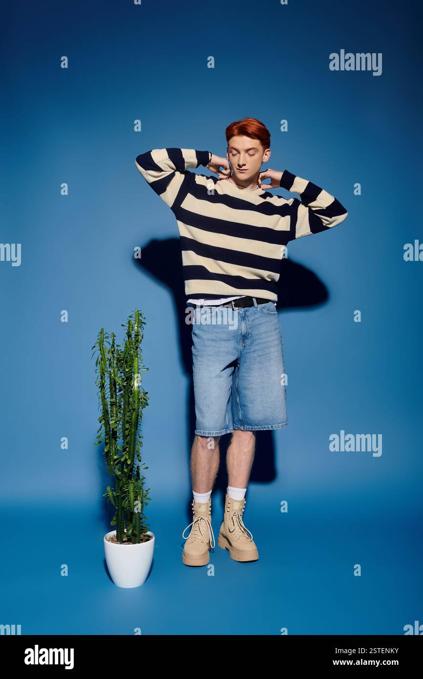 Ein junger Mann mit auffälligen Merkmalen bewegt sich in der Nähe einer Topfpflanze, verloren in tiefem Denken. Stockfoto