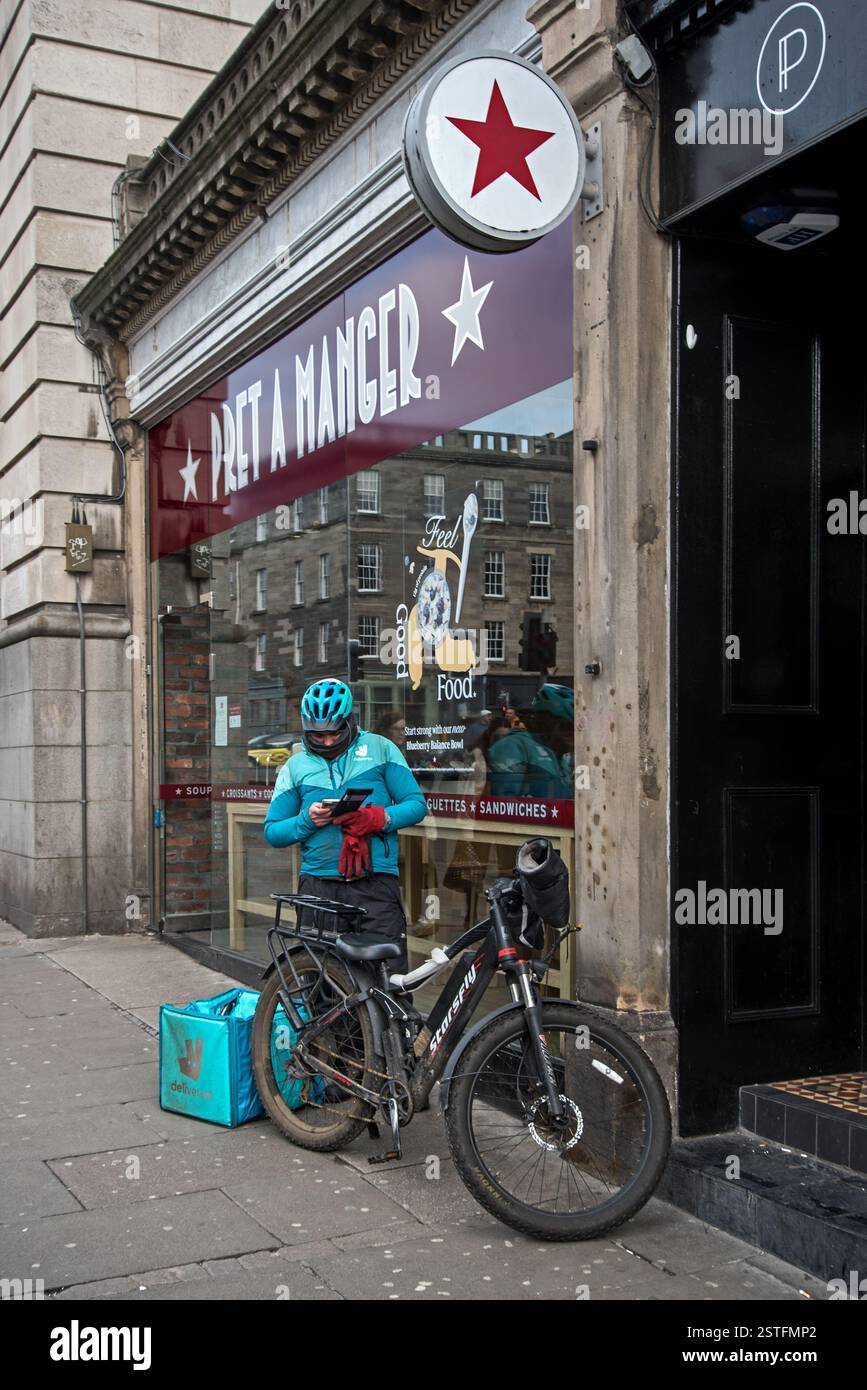 Deliveroo Essenskurier überprüft sein Handy vor einem Pret a Manger in Edinburgh, Schottland, Großbritannien. Stockfoto