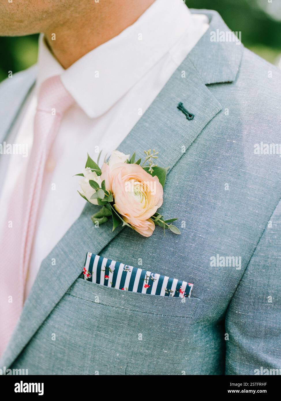 Ein Bräutigam trägt einen hellgrauen Anzug mit rosa Krawatte, Blumenboutonniere und gemustertem Taschenquadrat. Stockfoto