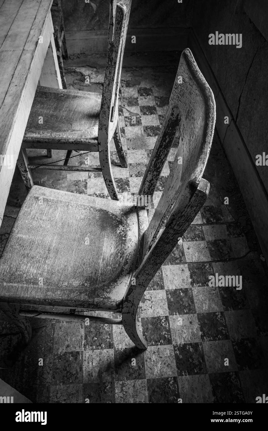 Holzstühle an einem Küchentisch mit Schachbrettboden in einer verlassenen Residenz in Bodie Geisterstadt. Stockfoto