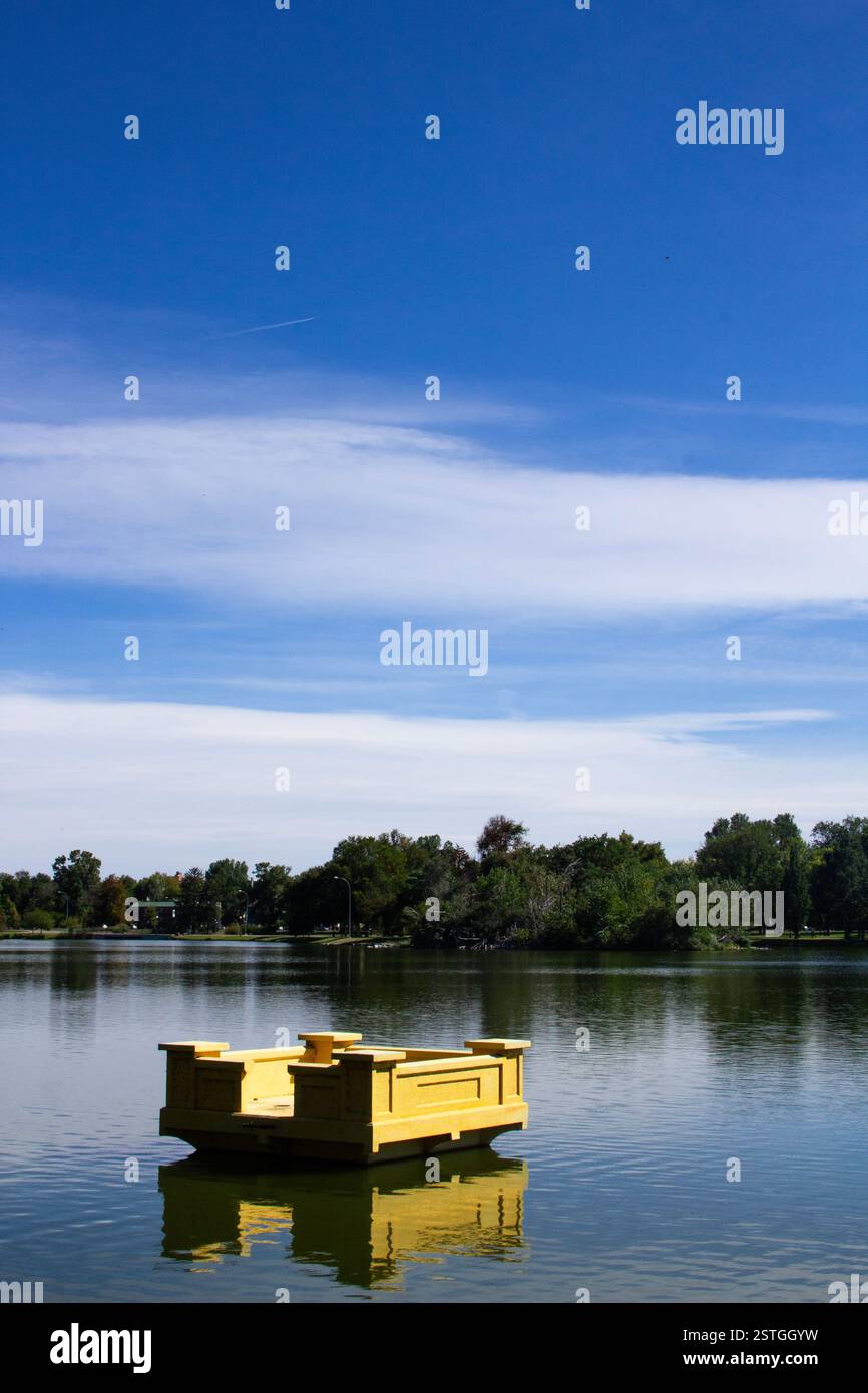 Eine schwebende gelbe rechteckige Skulptur, die auf einem See im Botanischen Garten von Denver schwimmt, mit dramatischem Kontrastlicht und klarem blauem Himmel Stockfoto