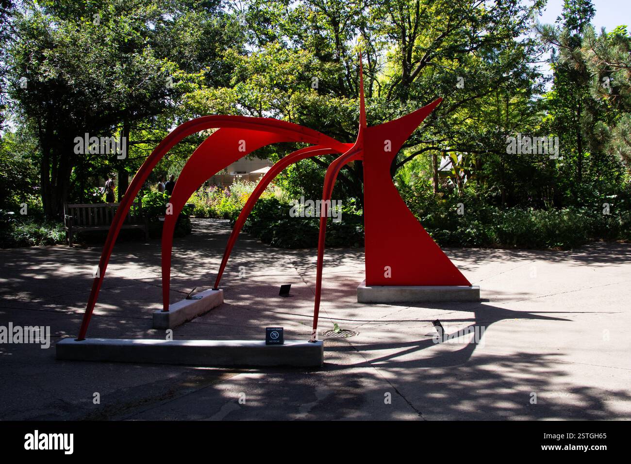 Die abstrakte Skulptur Calder in kräftigem Rot bildet einen auffälligen Kontrast zum Grün und dem Fußweg im Garten in Denver, Colorado. Stockfoto