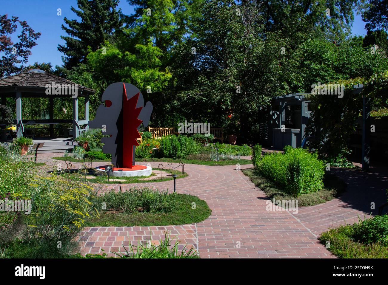 Eine auffällige rote Calder-Kopf- und Gesichtsskulptur steht im Kontrast zum umliegenden Grün des botanischen Gartens in Denver, Colorado. Stockfoto