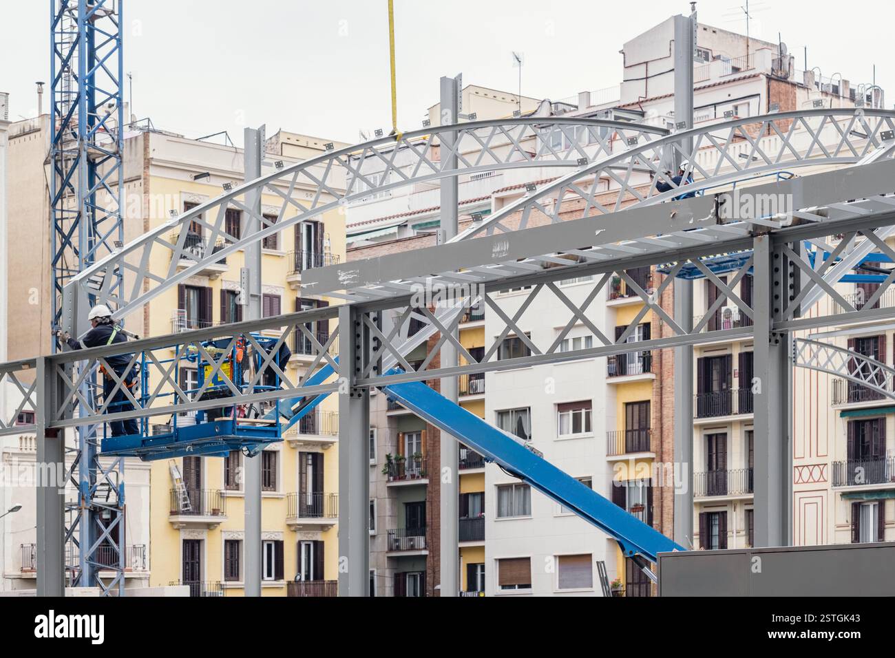 Bauarbeiter, die eine Hubarbeitsbühne und einen Kran verwenden, die gebogene architektonische Stahlträger auf der Baustelle installieren. Stockfoto