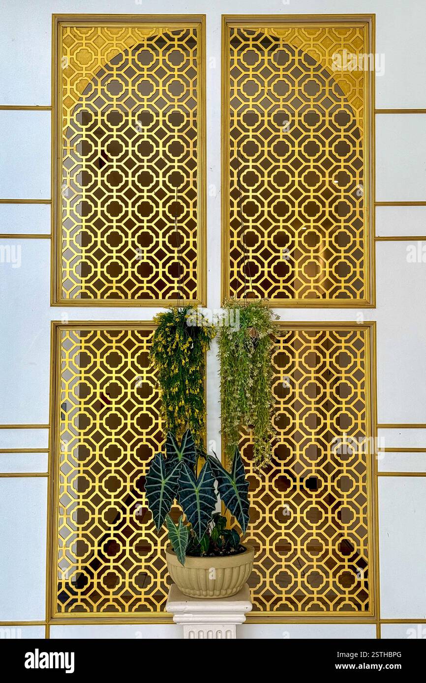 Goldenes Fenster mit geometrischen Mustern ein elegantes Fenster mit goldenen geometrischen Mustern, eingerahmt von einer weißen Fassade mit goldenen Details. Zwei Hangin Stockfoto