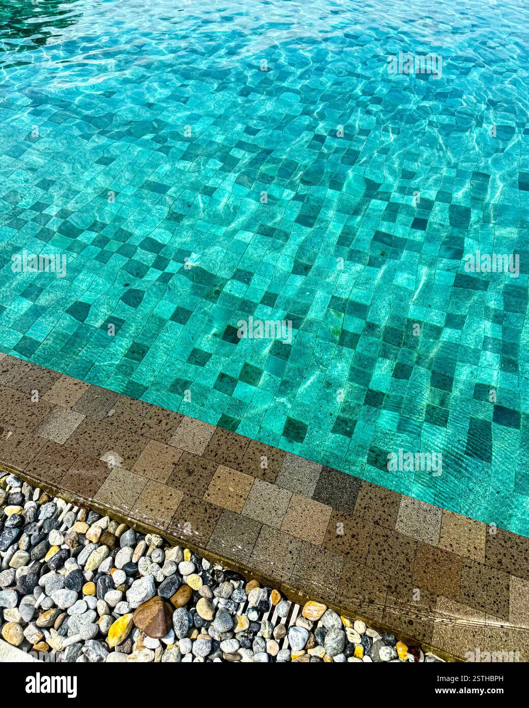 Mosaikfliesen Detail in einem Pool Nahaufnahme eines Swimmingpools mit grünen und blauen Mosaikfliesen, umgeben von natürlichen Kieselsteinen. Das kristallklare Wasser erzeugt - Smartphone-aufgenommenes Stockfoto