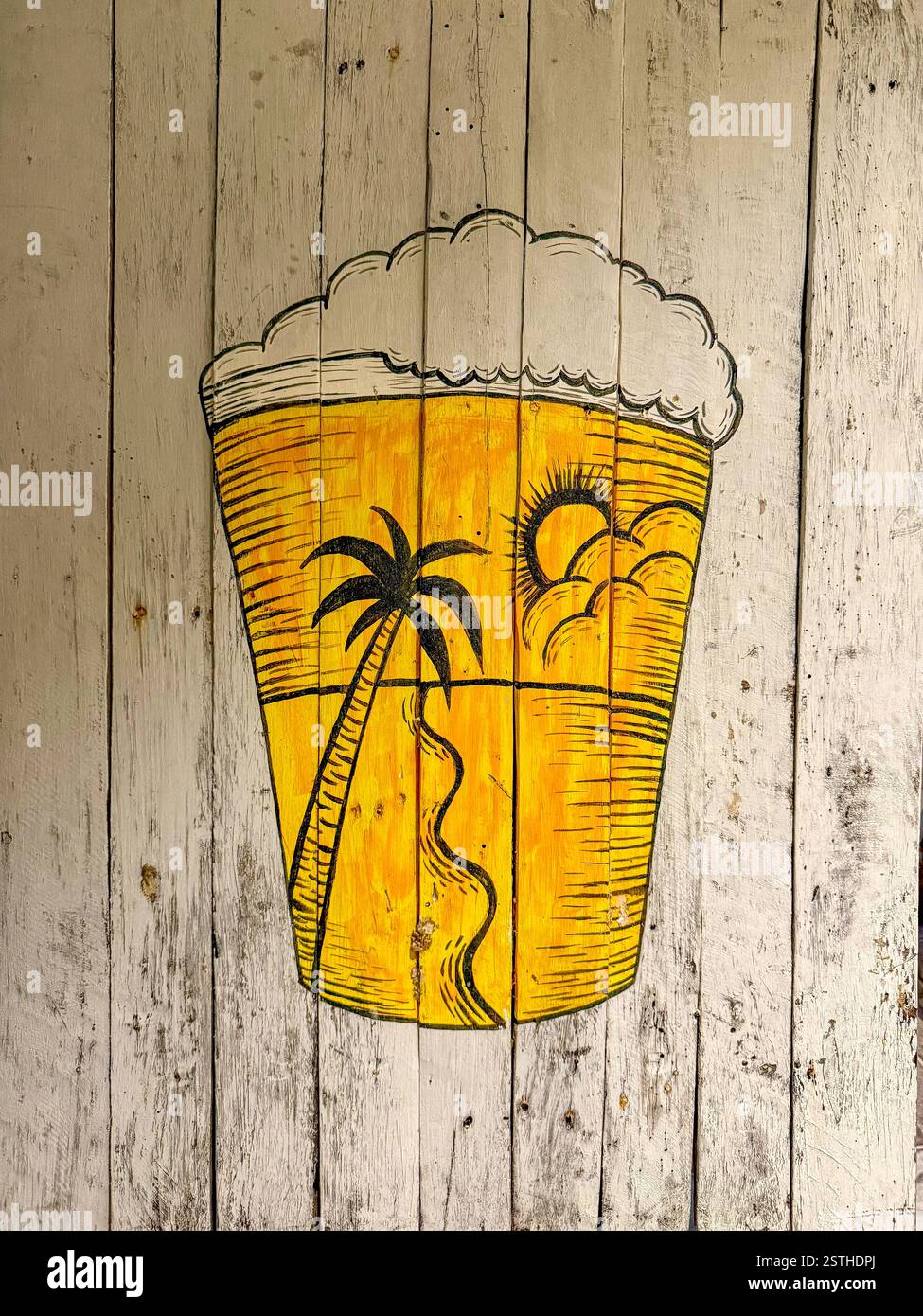 Erfrischendes Bier auf einem Holzbrett, Ein frostiges Glas Bier auf einer rustikalen Holzoberfläche, mit einer tropischen Palme, Sandstrand und Meer im - Smartphone-aufgenommenes Stockfoto