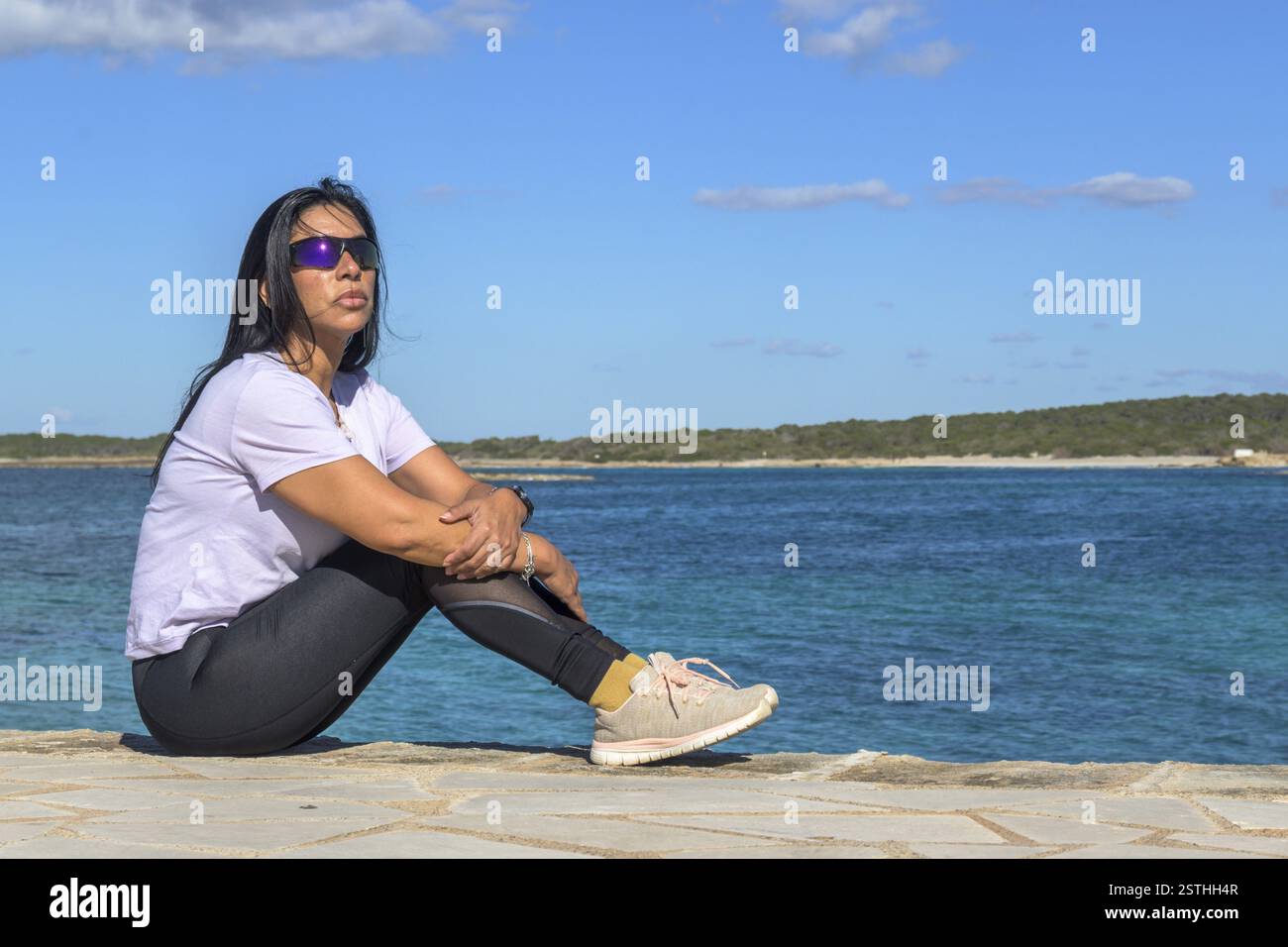 Frau sitzt am Meer, blickt in die Ferne, schöne Latina Frau am Meer in Colonia San Jordi, Balearen Inseln, Mallorca, Spanien, Europ Stockfoto