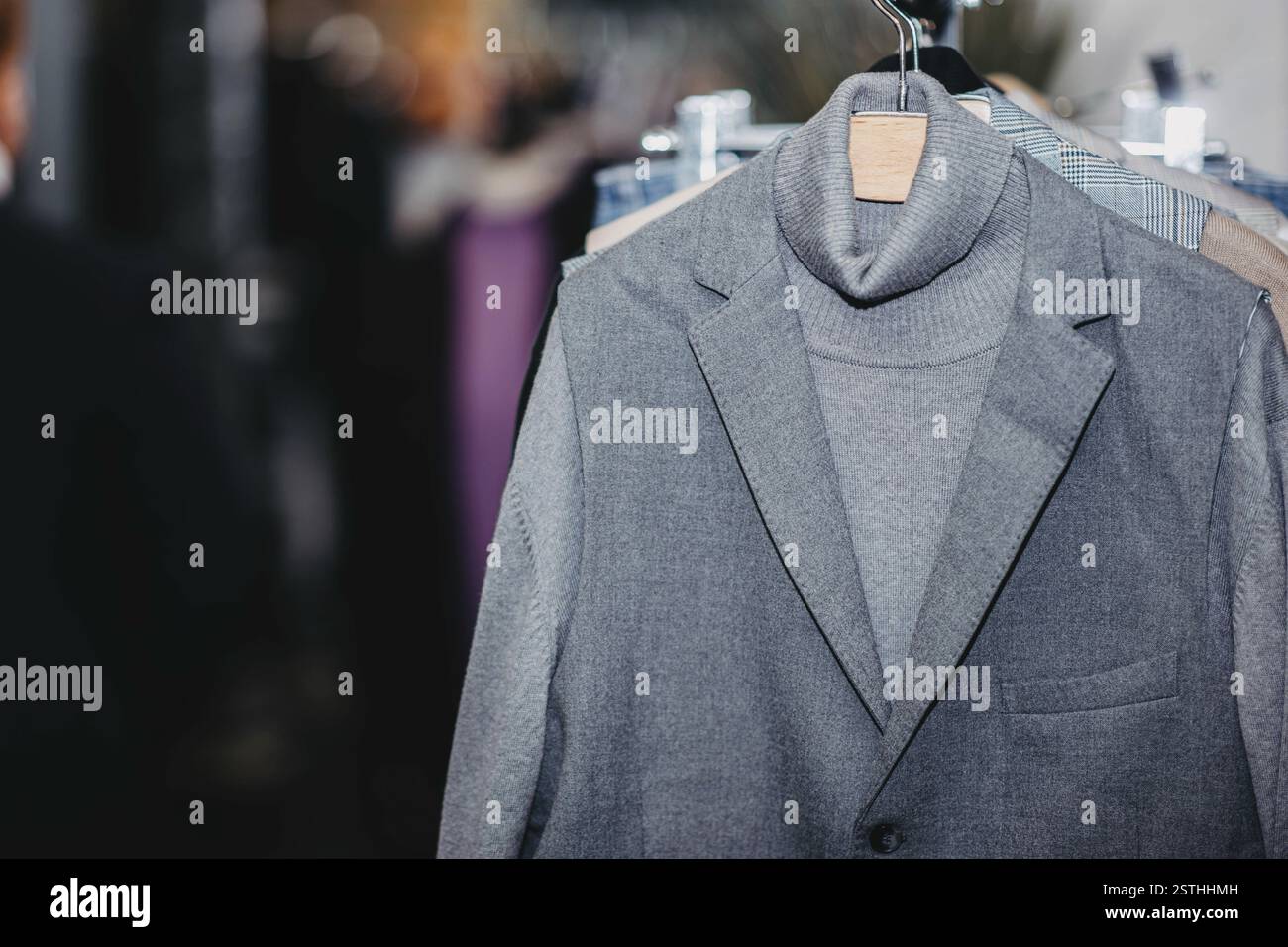 Ein eleganter grauer Anzug auf einem Kleiderbügel, der ordentlich in einem modischen neutralen Ton präsentiert wird Stockfoto