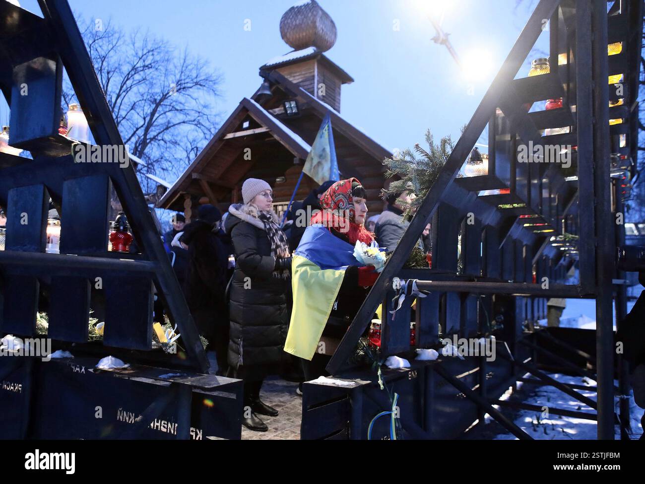 KIEW, UKRAINE - 18. FEBRUAR 2025 - Eine Frau wird während der Blumenverlegung zum Gedenken an die Helden des Hufens in die Flagge der Ukraine gewickelt Stockfoto