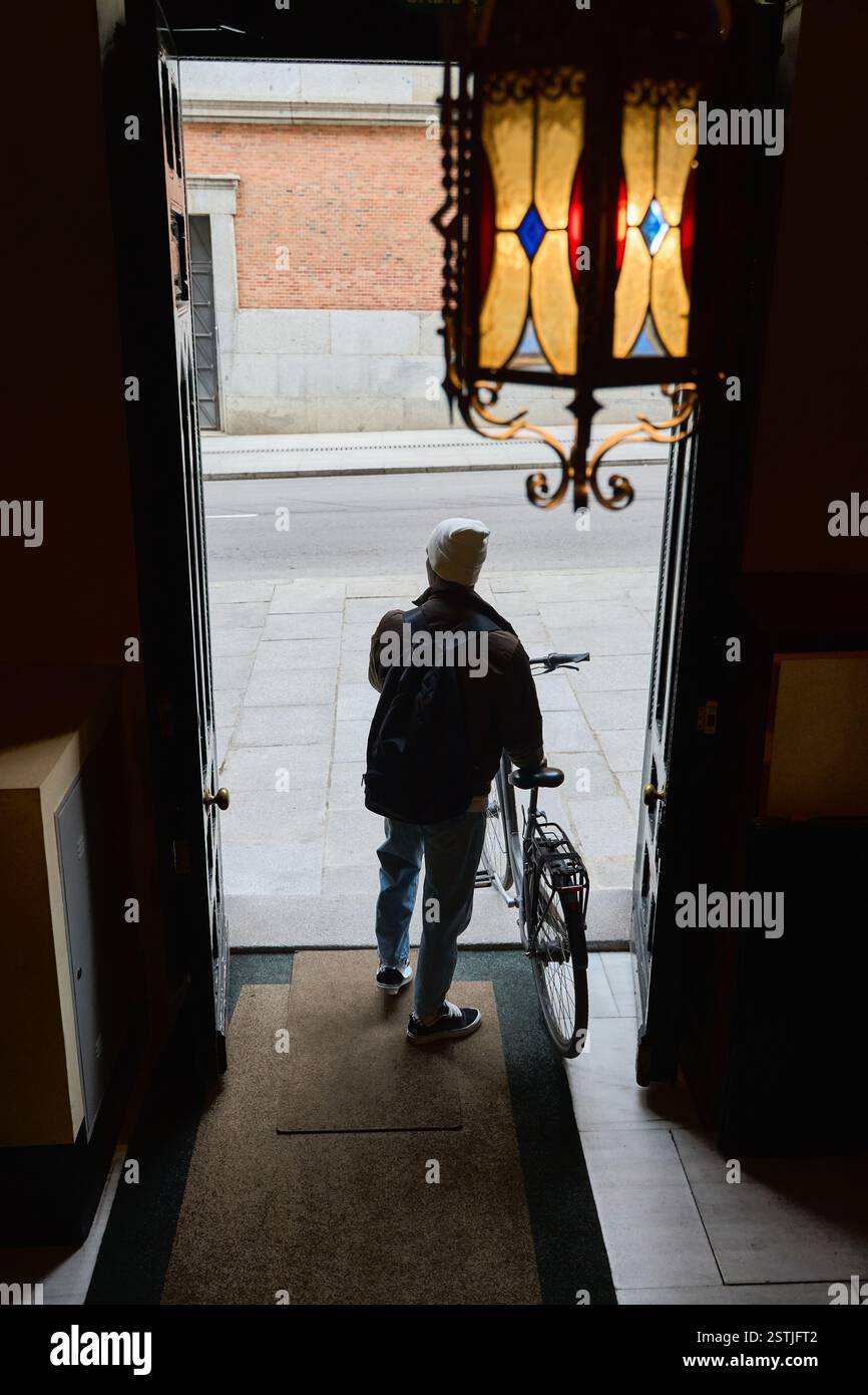 Ein junger Student, der mit seinem Fahrrad von hinten in ein Gebäude einsteigt, zeigt einen lässigen urbanen Lebensstil in einer pulsierenden Stadtkulisse Stockfoto