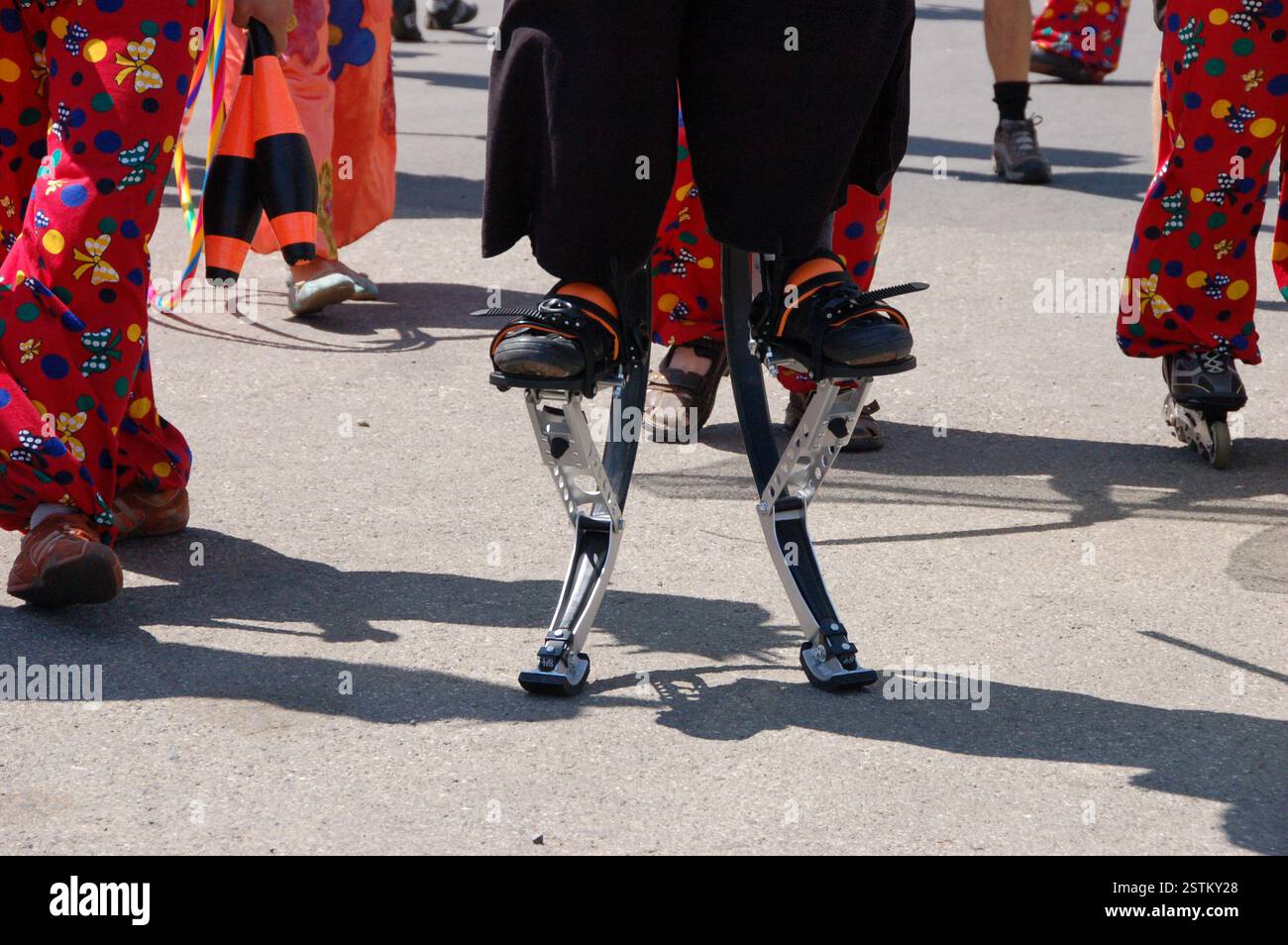 Festivalbesucher balancieren auf Metallstelzen und zeigen bei einer Veranstaltung im Freien ein einzigartiges und unkonventionelles Stelzendesign. Er trägt schwarze Hosen und Schuhe Stockfoto
