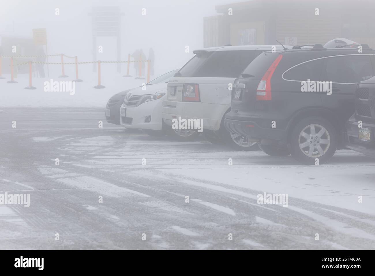 Schlechte Sicht, Autos parken an einem nebeligen Wintertag. Ein nebeliger Wintertag auf dem Parkplatz mit schneebedeckter Straße. Autos parkten auf einer nebeligen Winterstraße Stockfoto