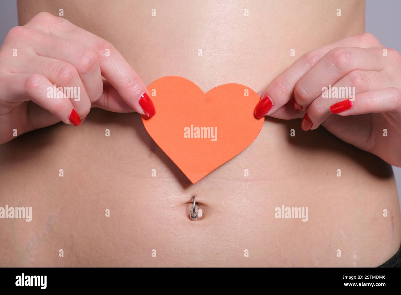 Orange Herz aus Papier auf schlanken Bauch Stockfoto