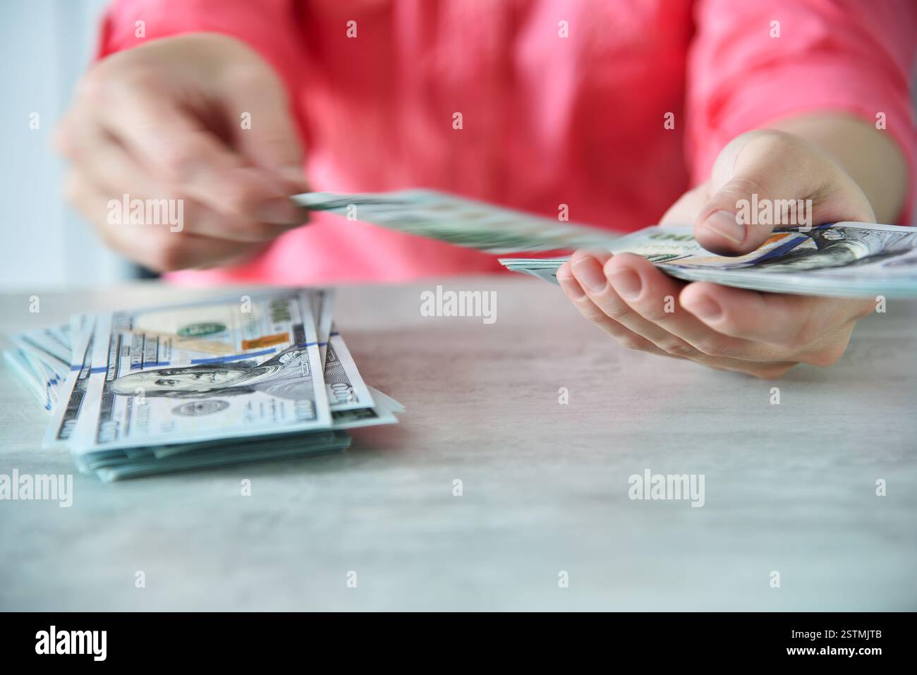 Rosafarbenes Frauenhemd zählt Dollar am Tisch. Finanzieller Erfolg und Geschäftskonzept. Nahaufnahme Stockfoto