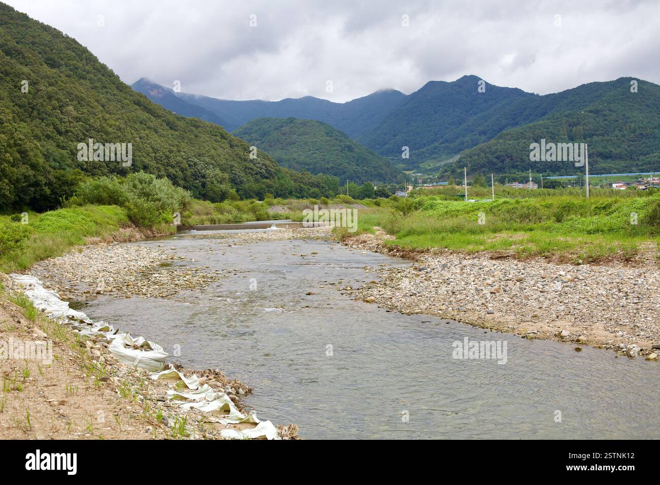 Goesan County, Südkorea – 10. September 2020: Ein flacher Fluss schlängelt sich durch ein Tal mit üppig grünen Bergen im Hintergrund und zeigt die Stockfoto