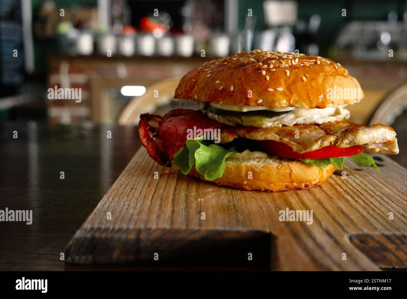 Burger mit gefliestem Ei und backon serviert auf Schneidebrett mit verschwommenem Pub-Innenraum im Hintergrund Stockfoto