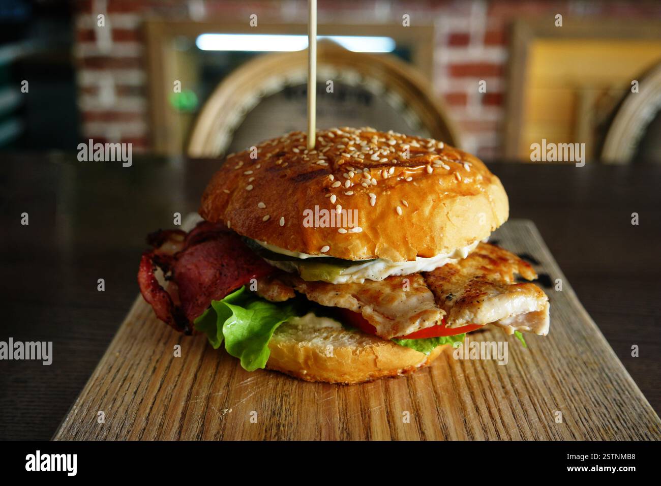 Gegrillter Burger mit backon und Salat, serviert auf Schneidebrett mit verschwommenem Pub-Innenraum im Hintergrund Stockfoto