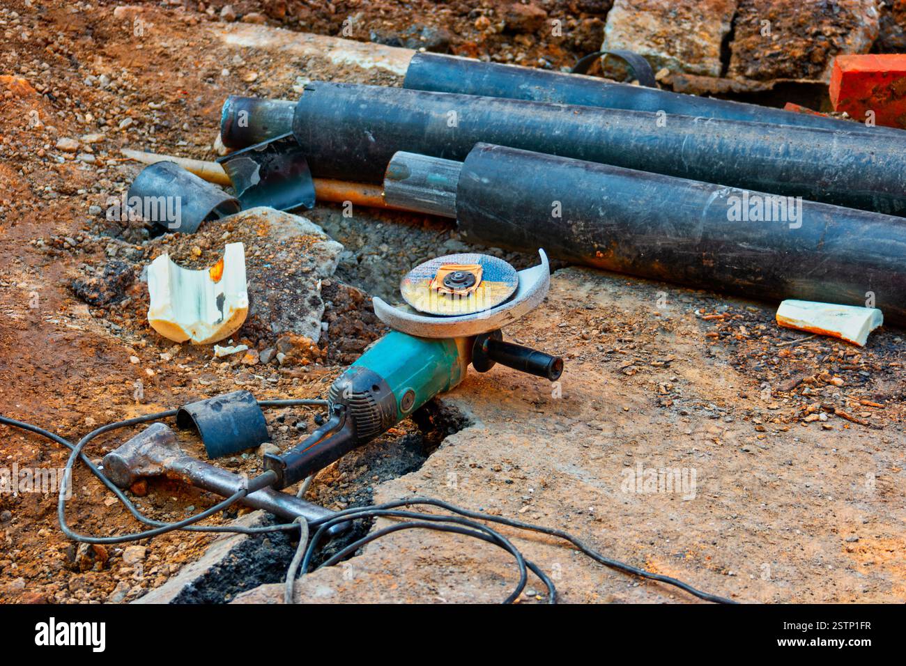 Der Winkelschleifer liegt auf der Erde in der Nähe von Wasserrohren, die mit PVC-Insylation bedeckt sind Stockfoto