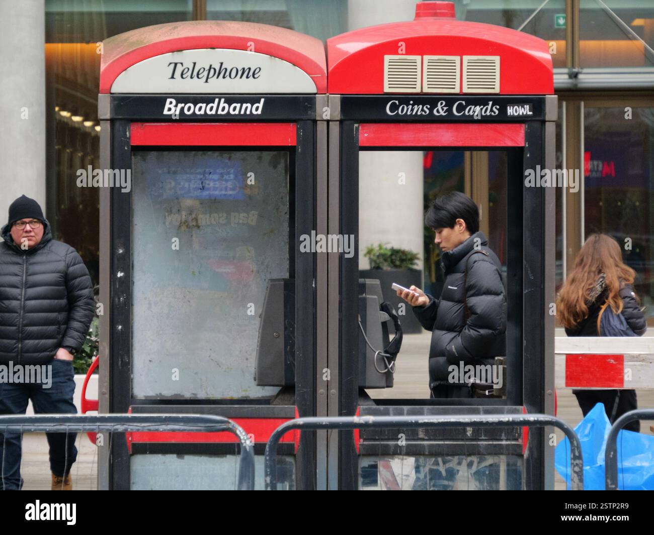 Mann eingerahmt von Telefonzelle mit fehlenden Fenstern, während er am Handy vorbeiläuft, Bishopsgate, London, Großbritannien Stockfoto