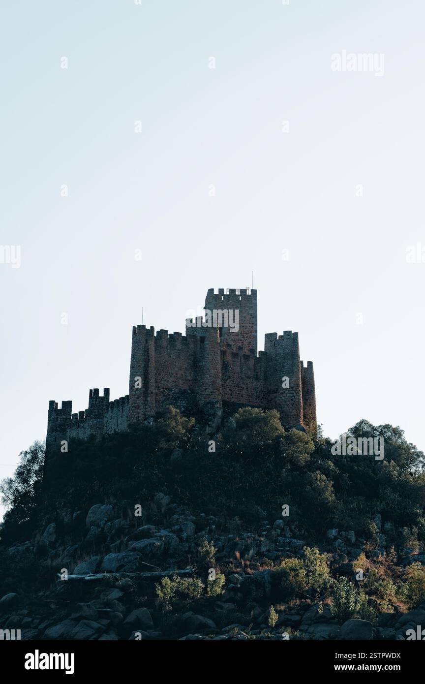 Almourol Castle erhebt sich über üppiges Grün und felsiges Gelände, das in sanftes Abendlicht getaucht ist Stockfoto