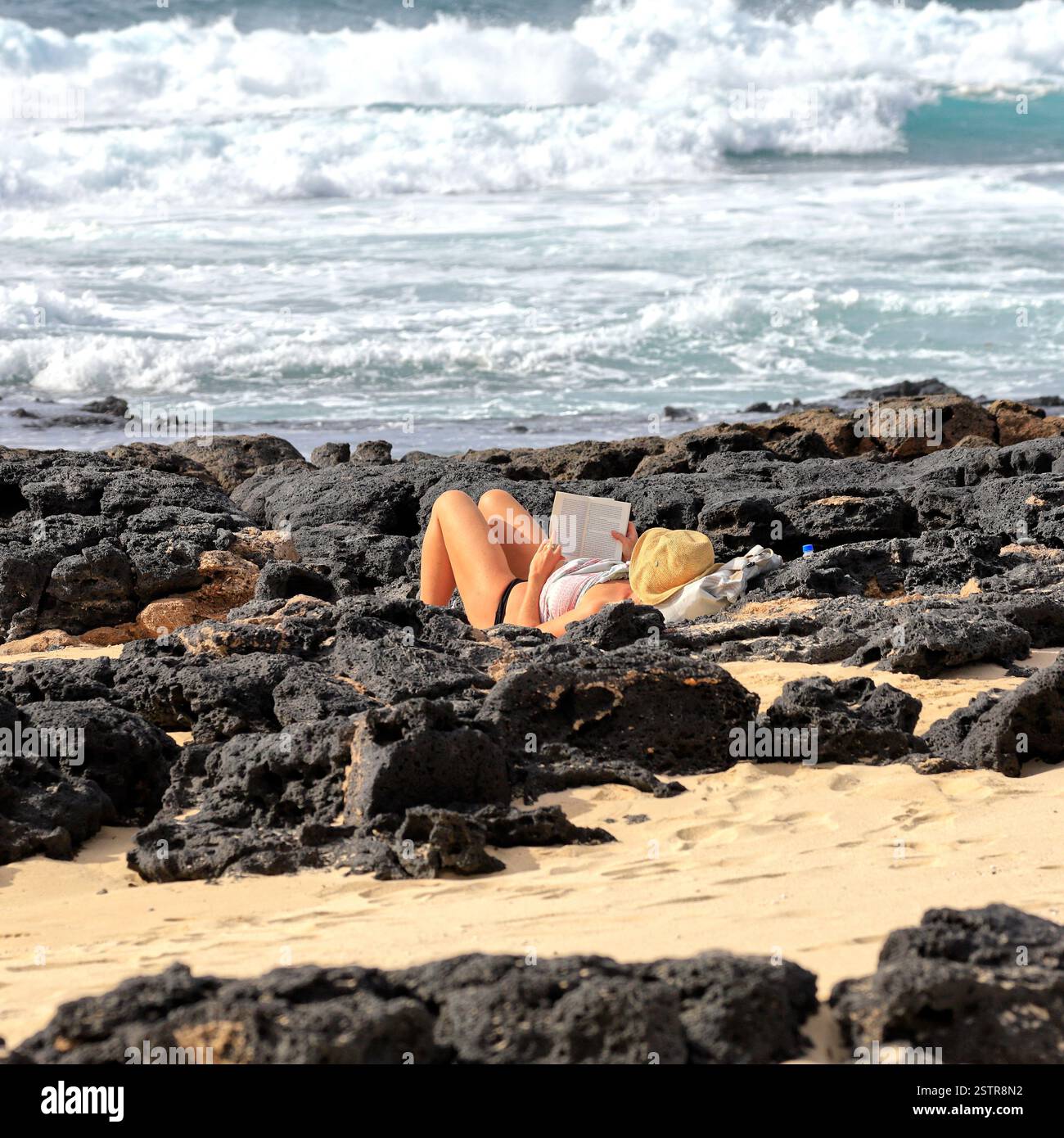 Frau, die Buch liest und sich zwischen vulkanischen Küstenfelsen entspannt, Fuerteventura, Kanarischen Inseln, Spanien, Europa, EU. Aufgenommen Im Dezember 2024 Stockfoto