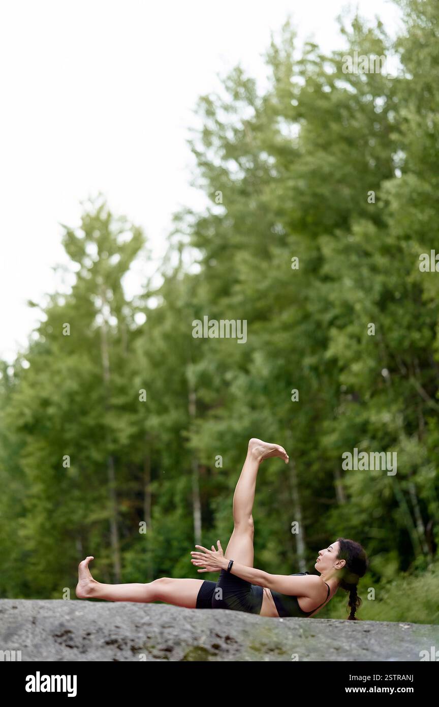 Yoga-Trainer liegt auf rosa Matte, übt Rückenhaltung von Hand bis Großzehe, ein Bein gerade nach oben gestreckt, das andere Bein horizontal gestreckt, tief gestreckt und Stockfoto