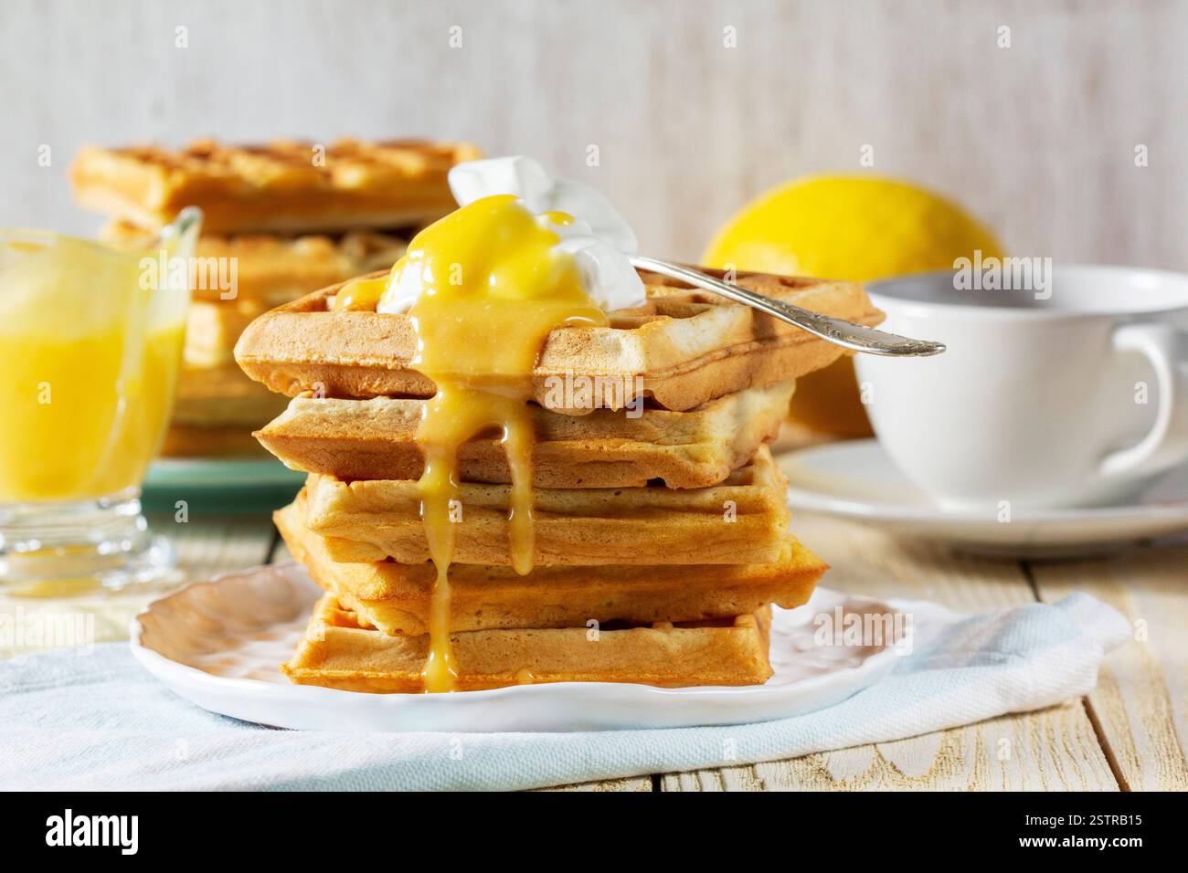 Belgische Waffeln mit Sahne und Zitronenquark, serviert mit Tee. Ein traditionelles Vergnügen für Karneval. Frühstück mit Waffeln mit Sahne auf hellem Hintergrund Stockfoto