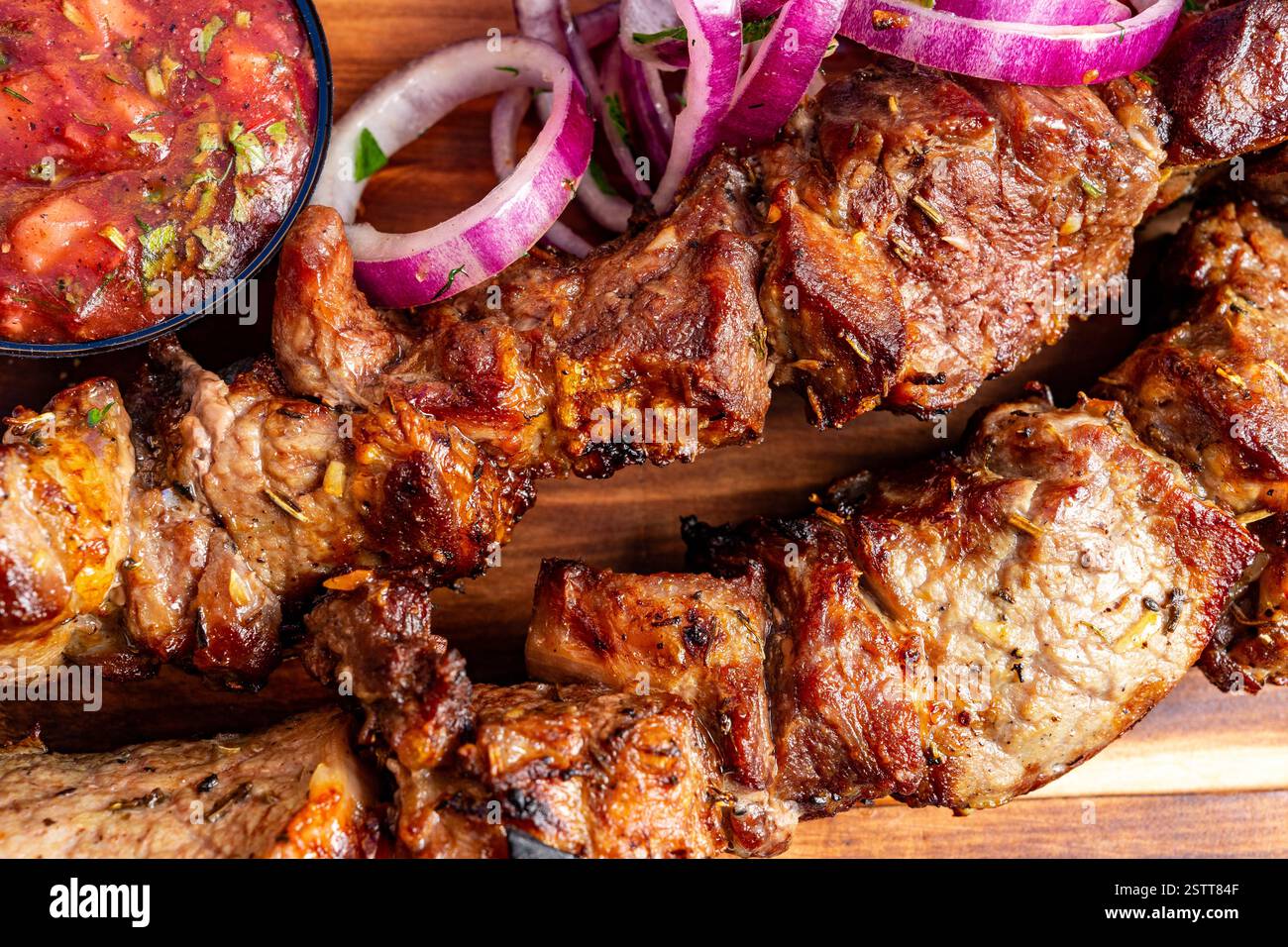 Saftiges gegrilltes Fleisch wird zusammen mit einer kleinen Schüssel frischer Salsa und dünn geschnittenen roten Zwiebeln serviert. Dieses appetitliche Gericht ist perfekt für einen herzhaften Abend Stockfoto
