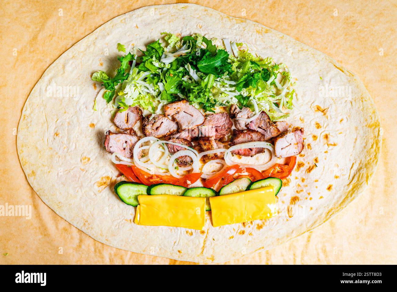 Eine große Mehltortilla wird mit Schichten von gegrilltem Fleisch, frischem Salat, Zwiebeln, Tomaten, Gurken, und Käse, bereit, in ein de gerollt zu werden Stockfoto
