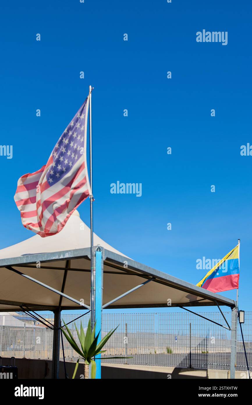 Flaggen der USA und Venezuelas schwenken Seite an Seite auf Fahnenmasten, mit einem klaren Himmel im Hintergrund. Ideal für Visualisierungen im Zusammenhang mit internationalen cooper Stockfoto