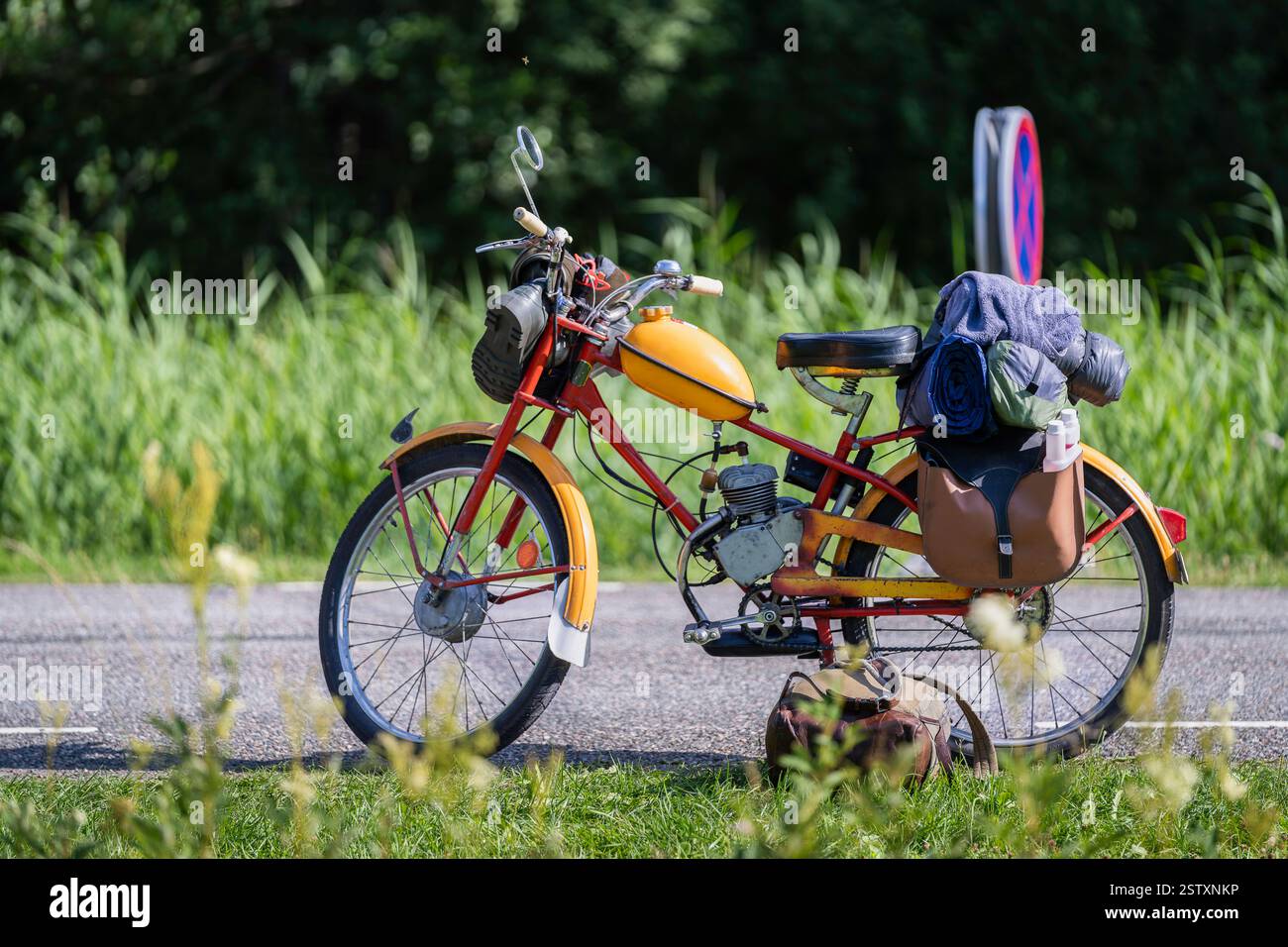 Gelbes und rotes Oldtimer-Moped, Rennrad steht auf der Straße. Ein altes Moped mit Satteltaschen und Gummibändern. Sommerreise auf einem Moped. Stockfoto