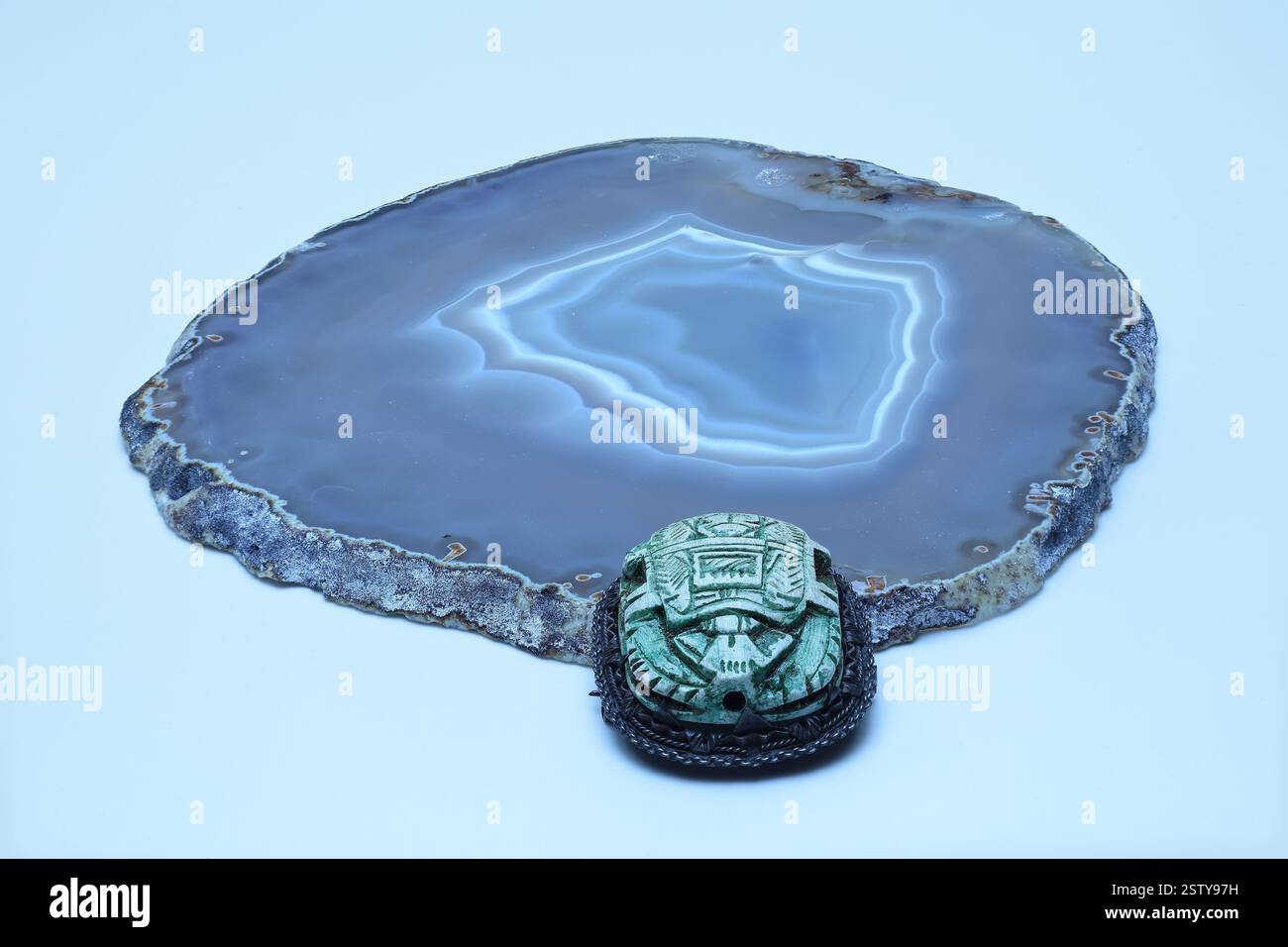 Stillleben: Brosche mit geschnitzten Symbolen auf einem ägyptischen Scarab. Der Käfer steigt aus einem Stück Achat ab. Nahaufnahme auf hellem Hintergrund mit großer Tiefe Stockfoto