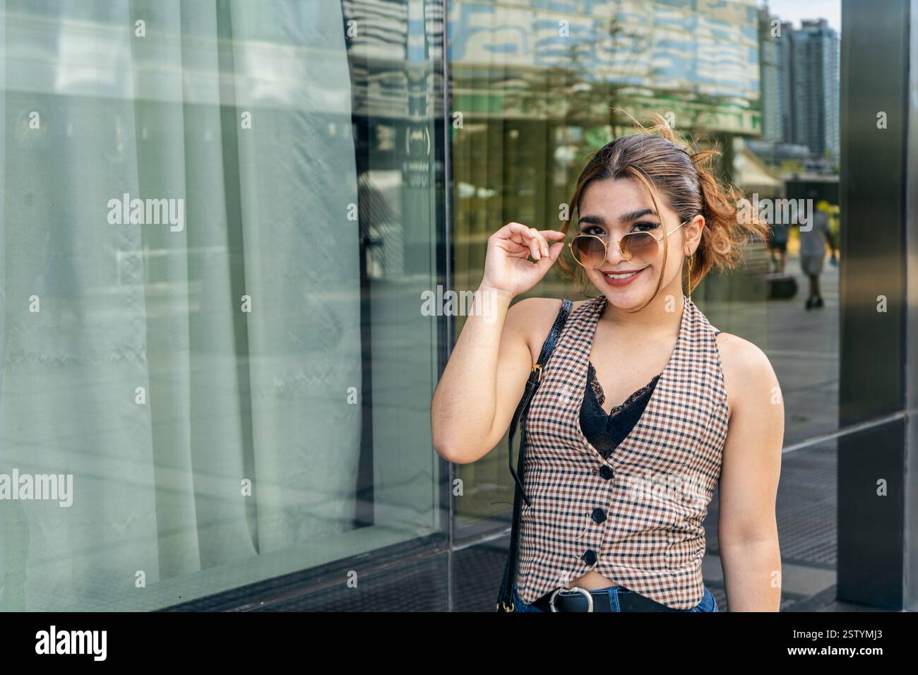 Stilvolle junge Frau lächelt im Freien in urbaner Umgebung Stockfoto