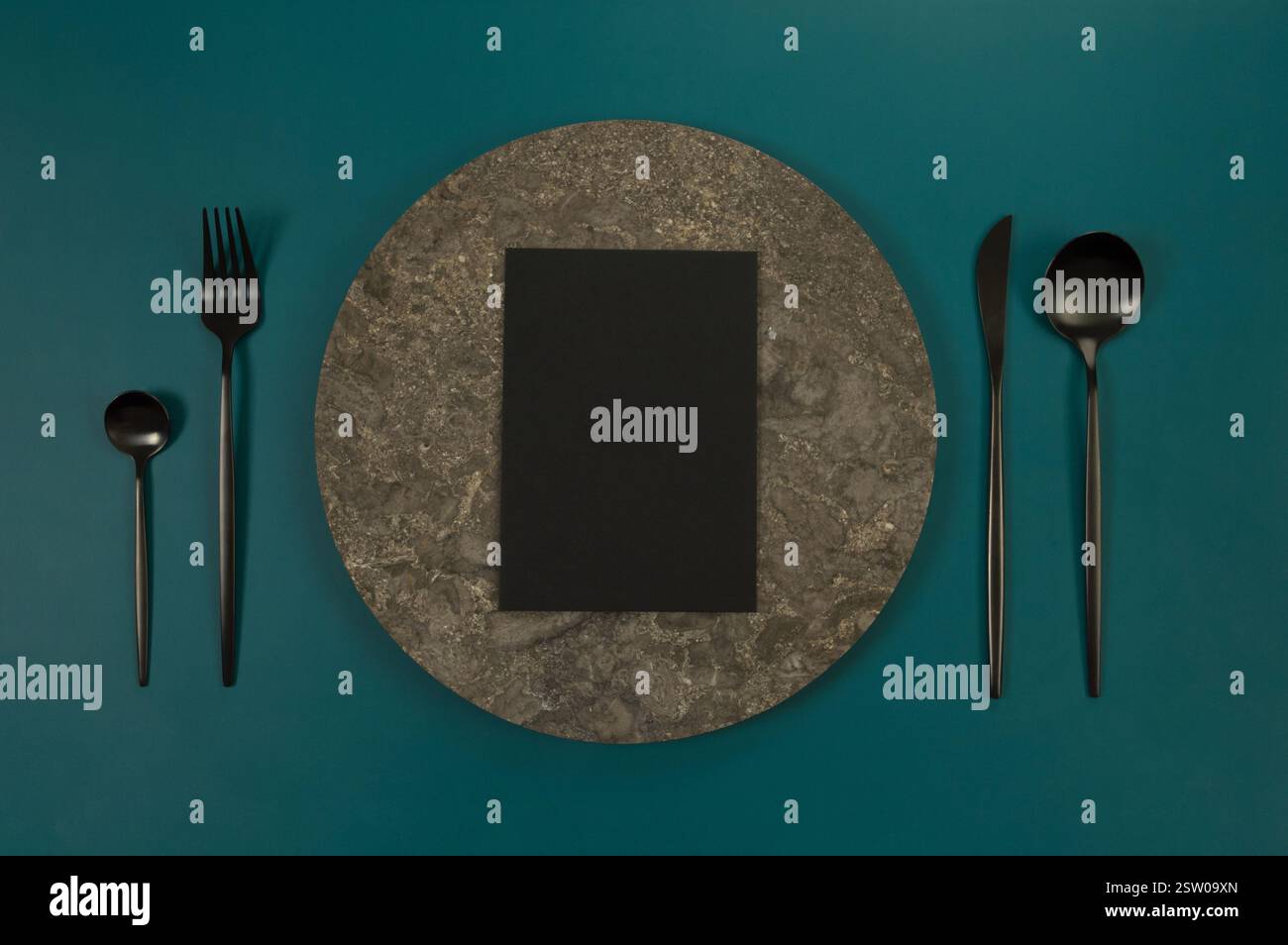 Blick von oben auf braunen Marmorteller, schwarzes Besteck und schwarze Karte auf dunkelgrünem Hintergrund. Essenspräsentation, Steintablett. Tabelleneinstellung, Kopierbereich. Stockfoto