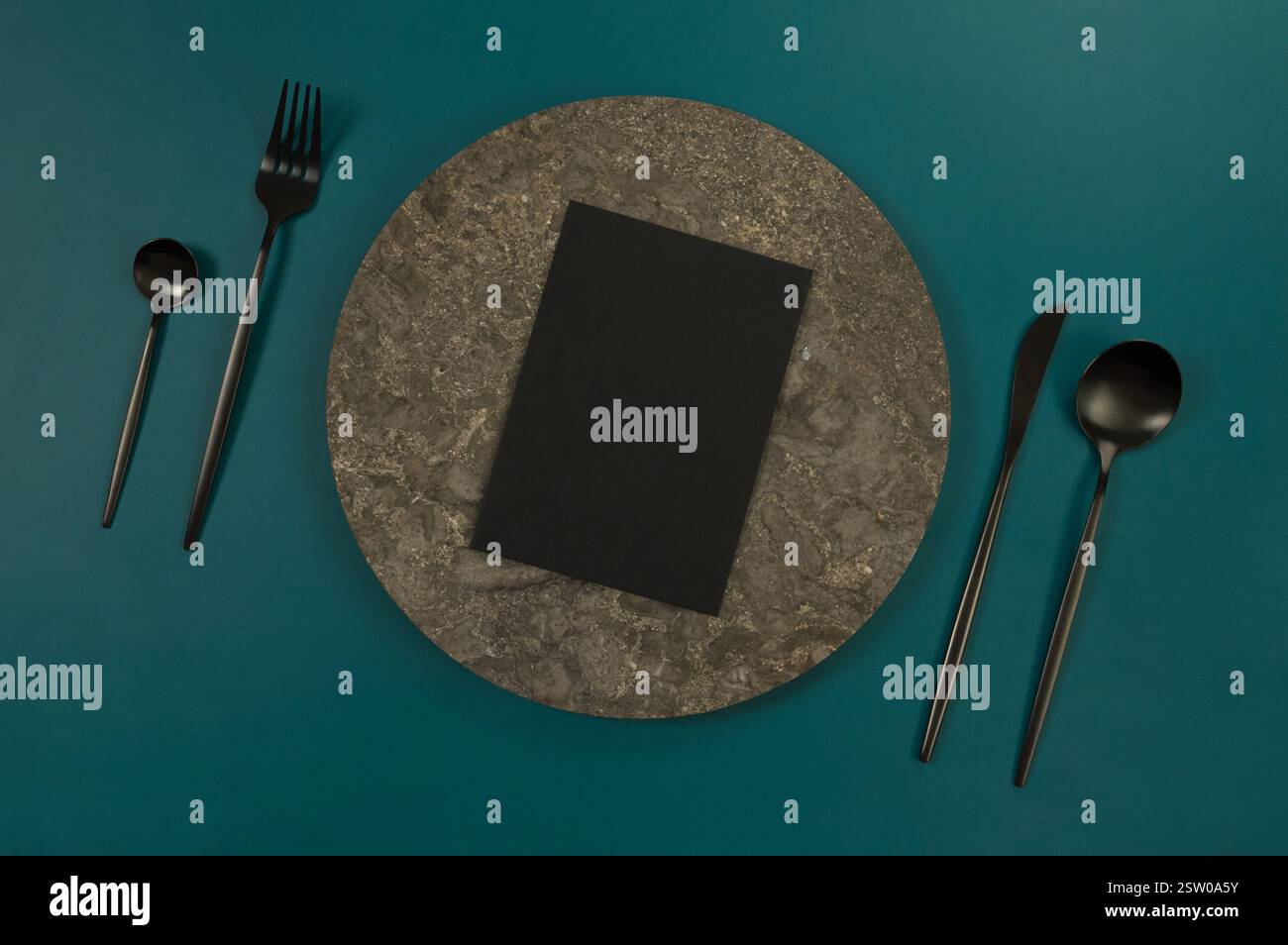 Blick von oben auf braunen Marmorteller, schwarzes Besteck und schwarze Karte auf dunkelgrünem Hintergrund. Essenspräsentation, Steintablett. Tabelleneinstellung, Kopierbereich. Stockfoto
