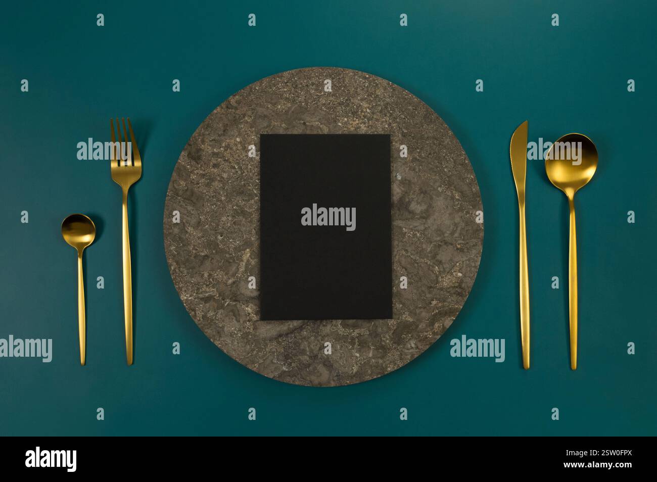 Blick von oben auf braunen Marmorteller, goldenes Besteck und schwarze Karte auf dunkelgrünem Hintergrund. Essenspräsentation, Steintablett. Tabelleneinstellung, Kopierbereich. Stockfoto